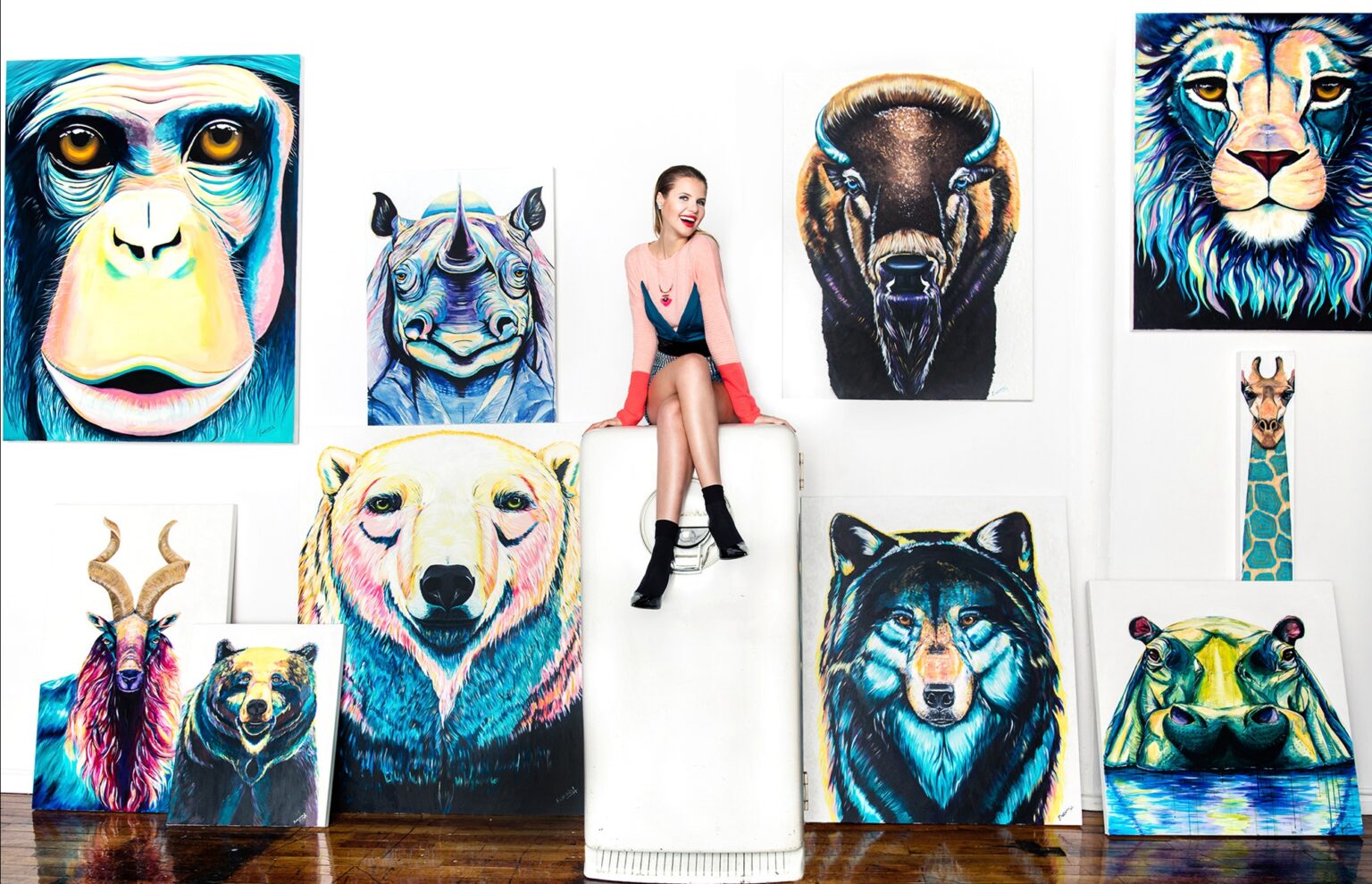 Ekaterina Sky seated among her Animalize paintings of a chimpanzee, rhino, bison, lion, polar bear, wolf, giraffe and hippo